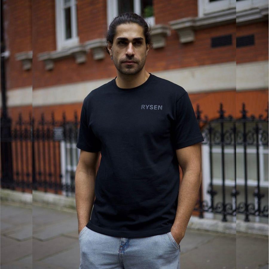 RYSEN First Edition Tee in black, tonal Minimal mark, worn against a London brick terrace